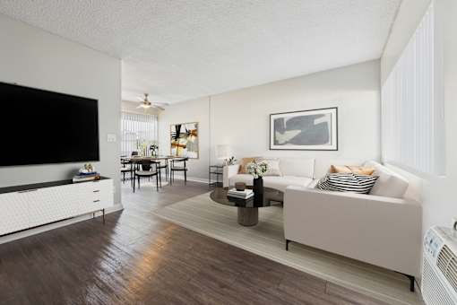 A living room with a white couch, a wooden floor, and a flat screen TV mounted on the wall.