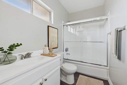 A white bathroom with a toilet, sink, mirror, and shower.