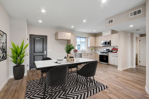 a dining area with a table and chairs and a kitchen in the background