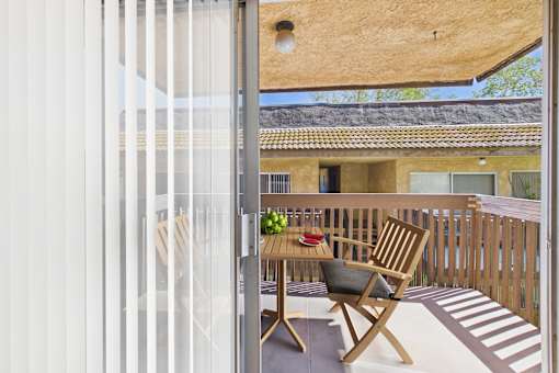 A wooden chair is on a patio with a table in front of a house.
