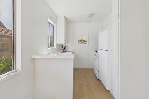 A small white kitchen with a fridge, sink and window.