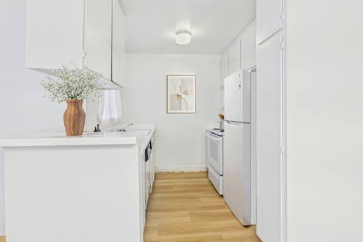 A kitchen with white appliances and a wooden floor.