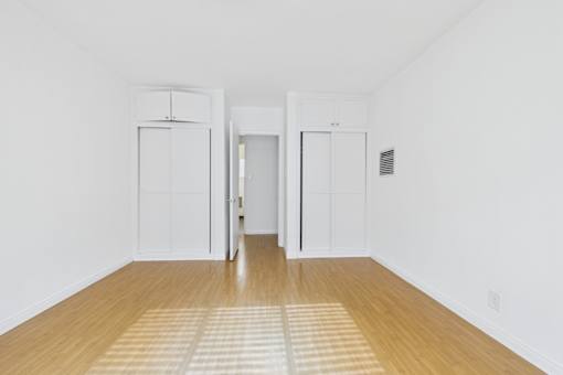 A room with white walls and wooden flooring with two white doors.
