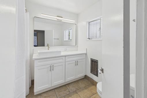 A white bathroom with a sink, mirror, and toilet.