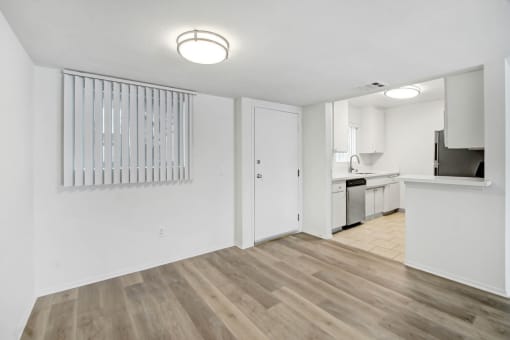 an empty living room and kitchen with white walls and wood flooring