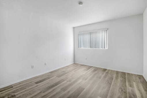 a bedroom with white walls and wood flooring and a window