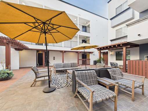 A yellow umbrella is on a patio with chairs and tables.