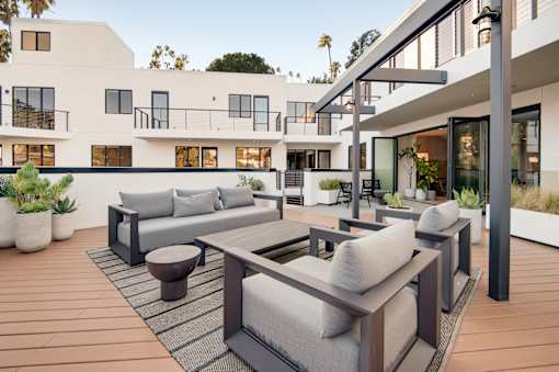 A modern outdoor seating area with a wooden floor and grey cushions.