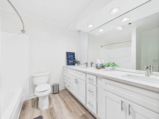 A white toilet is in a bathroom with a white sink and white cabinets.