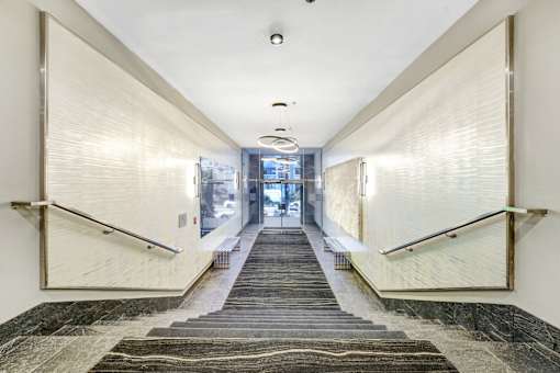 A long hallway with a carpeted staircase and a metal railing.