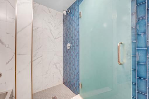 A shower area with a glass door and a marble wall.
