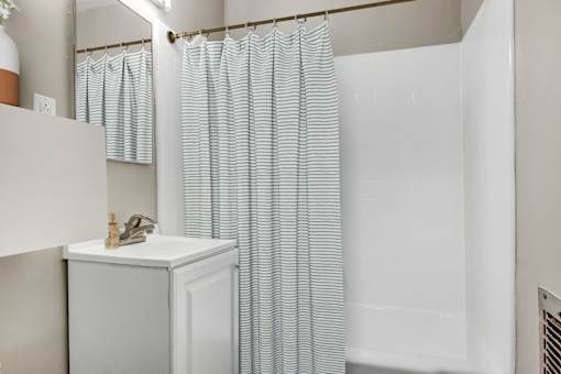 A white cabinet with a plant on top is next to a shower curtain.