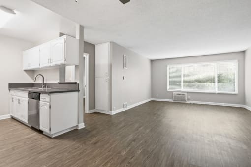 an empty living room with a kitchen and a window