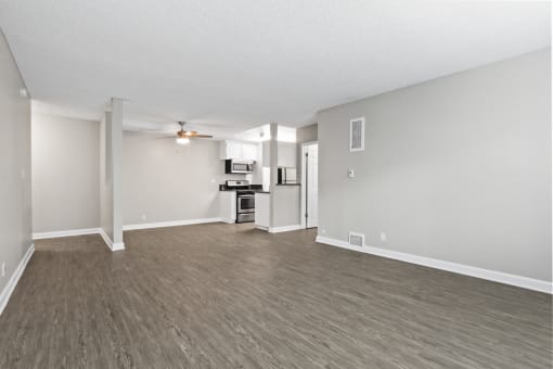 the living room and kitchen of an apartment with wood flooring and a ceiling fan