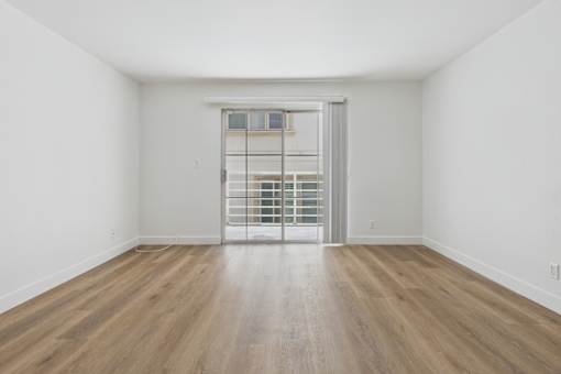 A room with wooden floors and a door leading to a balcony.