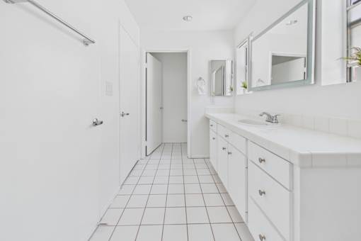 A white bathroom with a sink, mirror, and tiled floor.