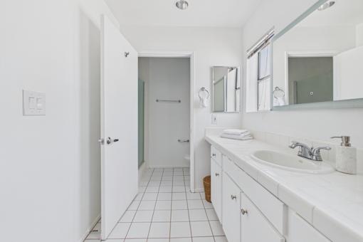 A white bathroom with a sink, mirror, and toiletries.