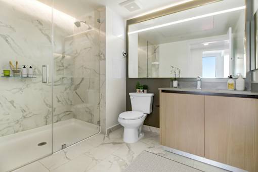 A white toilet sits in a marble bathroom next to a walk-in shower.