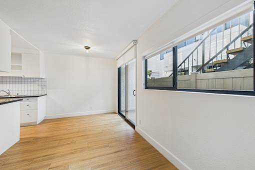 A room with a wooden floor and a staircase outside.