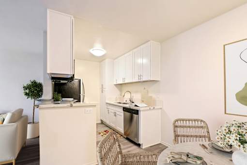A modern kitchen with white cabinets and appliances, a dining table with chairs, and a potted plant.