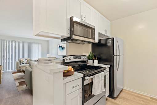 A black refrigerator is in a white kitchen with a stove and microwave above it.