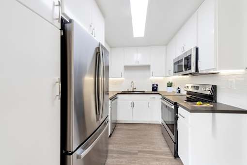 A modern kitchen with a stainless steel refrigerator and black countertops.