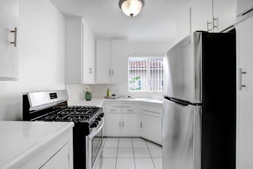 A black refrigerator stands in a kitchen with white cabinets and appliances.