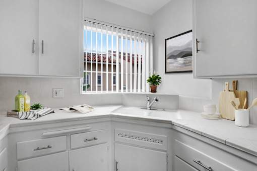 A kitchen with white cabinets and a window with blinds.
