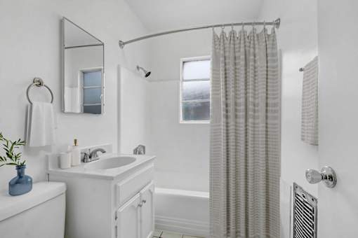 A white bathroom with a blue vase on the sink.