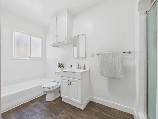 A white bathroom with a wooden floor and a window.