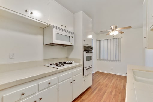 Kitchen with white gas cooktop over microwave, White Oven, Wood Style floors throughout dining area with ceiling fan