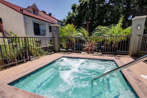 A hot tub sits in the middle of a patio surrounded by a fence.
