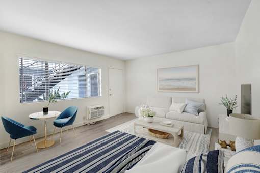 A living room with a white couch, blue chairs, and a painting on the wall.