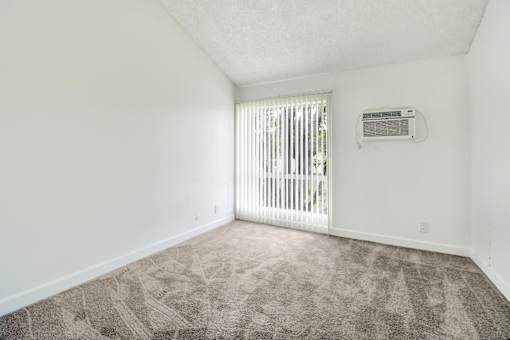 A room with a carpeted floor and a window with blinds.