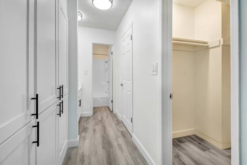 A hallway with white cabinets and a light brown floor.