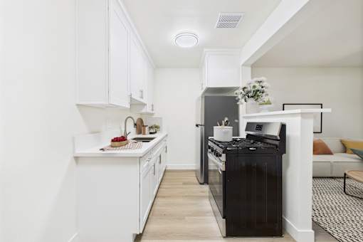 A black fridge sits in a white kitchen next to a white counter.