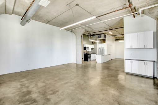 an empty room with white walls and concrete floors and a kitchen
