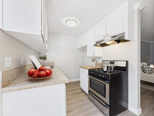 A kitchen with a black stove top oven and a bowl of red apples on the counter.