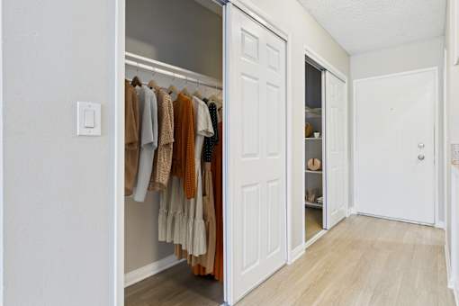 A white closet with clothes hanging and a shelf with shoes.
