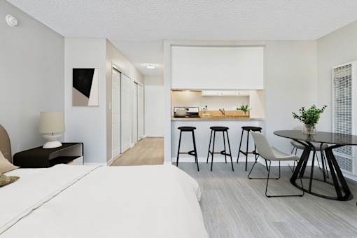 A modern bedroom with a large bed and a kitchen area in the background.