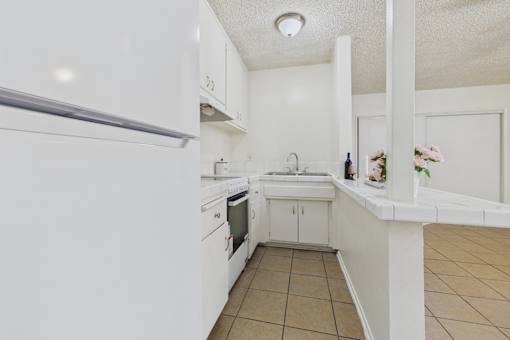 A white kitchen with a refrigerator on the left and a sink in the middle.