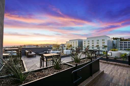 A rooftop patio with a table and chairs overlooking a cityscape at sunset.