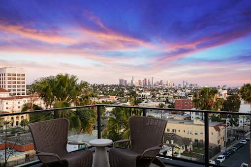 Two chairs and a table are set up on a balcony overlooking a city skyline.