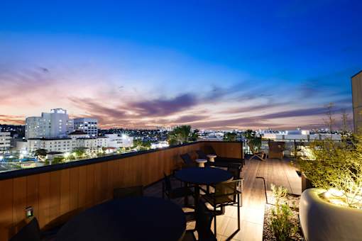 A rooftop patio with tables and chairs overlooking a cityscape at dusk.