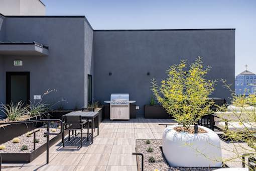 A modern outdoor patio area with a table, chairs, and a tree at Skylar At Sunset Apartments, Los Angeles, CA, 90027