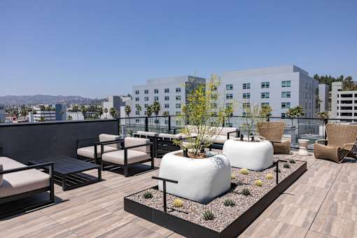 A rooftop patio with white chairs and tables at Skylar At Sunset Apartments, Los Angeles 90027