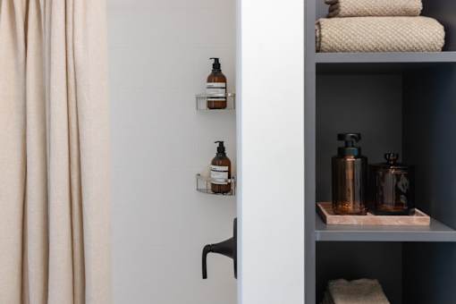 A bathroom with a white wall and a grey shelf with towels and bottles on it at Skylar At Sunset Apartments, California