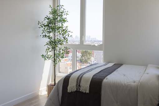 A bedroom with a bed and a plant by the window at Skylar At Sunset Apartments, Los Angeles, California