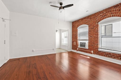 an empty living room with hardwood floors and a brick wall