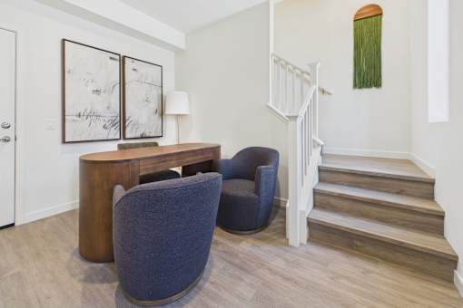 A chair sits in a room with a staircase and a painting on the wall.